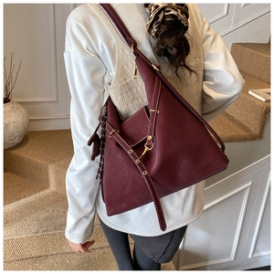 Detail of burgundy leather shoulder bag featuring white contrast stitching and gold hardware