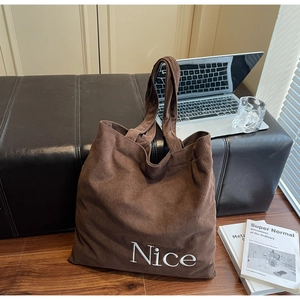Close-up of brown corduroy tote bag with Nice embroidery on black leather bench
