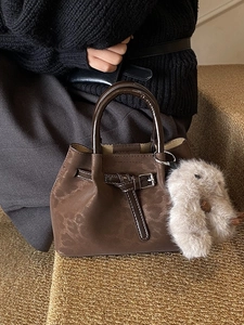 Retro dark brown bucket bag with smooth handles and a plush rabbit charm accessory
