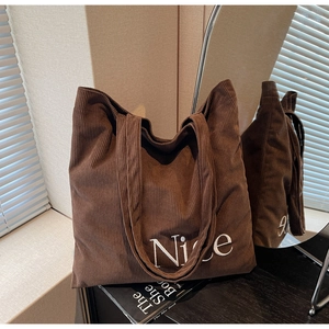 Detailed texture of brown corduroy tote bag featuring white embroidered Nice lettering