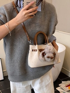 Chic beige bucket bag with brown handles and plush bunny charm worn as a crossbody