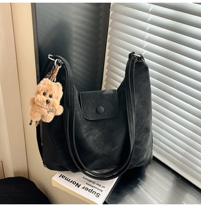 Close-up of black vintage shoulder bag with textured leather and plush puppy charm