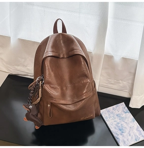 Détail du sac à dos en cuir marron avec un pendentif chien et une poche zippée