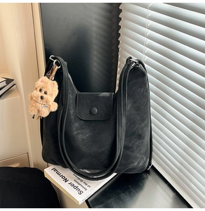 Detail view of black faux leather tote bag with magnetic clasp and cute plush puppy charm