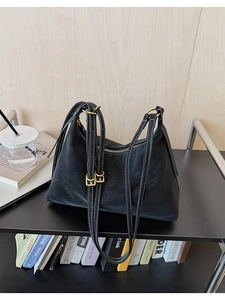 Detail of matte black shoulder bag featuring white contrast stitching and gold metal rings