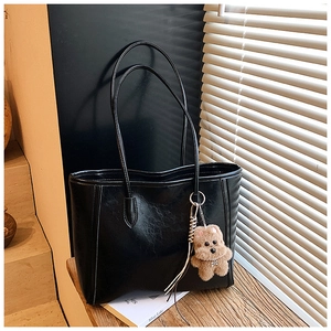 Detail of black PU leather tote bag with elegant texture and a brown plush bear charm