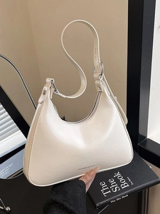 Chic cream white half-moon hobo bag with adjustable strap and silver buckles on a book