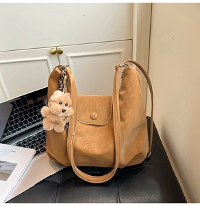 Detail view of brown faux suede tote bag featuring a flap closure and cute plush bear charm