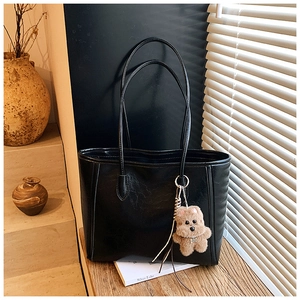 Detail of black leather tote bag with a cute brown teddy bear pendant on wooden table
