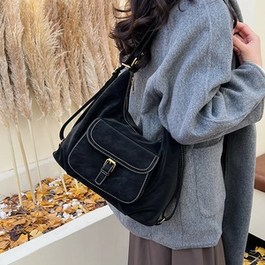 Detail of black leather hobo bag with contrast stitching and metal buckle on front pocket