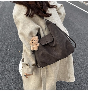 Detail of a large brown suede shoulder bag with a teddy bear charm on a beige coat