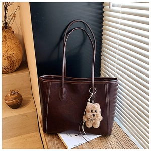 Detail of dark brown leather tote bag with a cute plush puppy pendant in warm studio light