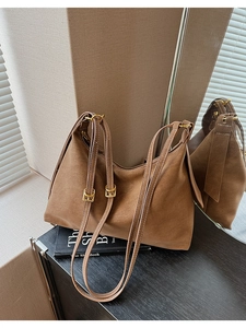 Close-up of brown suede tote bag featuring adjustable shoulder straps and gold buckles