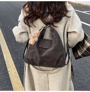Detail of dark brown vintage faux leather shoulder bag with plush bear charm accessory