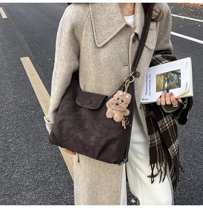 Outdoor shot of a vintage brown tote bag with a plush bear charm on a beige coat model