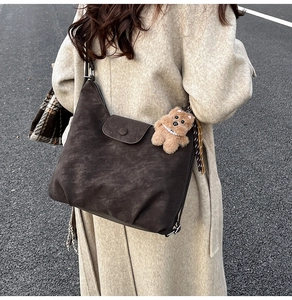 Detail of a dark brown suede tote bag featuring a decorative flap and plush bear charm
