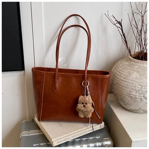 Detailed close-up of brown faux leather tote bag with cute plush bear charm on a silver suitcase