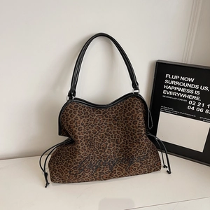 Detail of leopard print tote bag featuring black leather handles and cursive embroidery