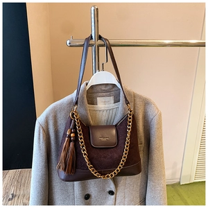 Détail du sac bandoulière en daim marron avec chaîne dorée et gland sur un manteau gris