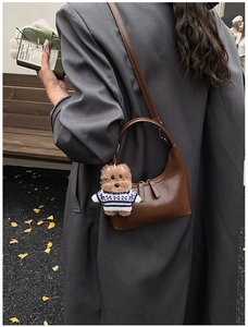 Détail du sac demi-lune en cuir marron avec breloque chiot en peluche et bandoulière