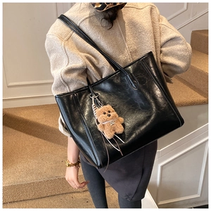 Detail of black PU leather tote bag with a cute brown teddy bear pendant and long straps