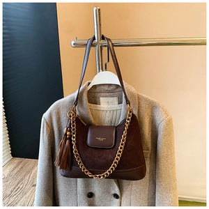 Détail du sac en daim marron avec chaîne dorée et inscription HUGHER & BAGS sur manteau