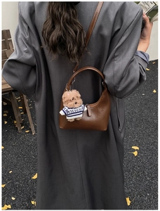 Détail du sac hobo en cuir marron avec breloque ours en peluche porté par un mannequin