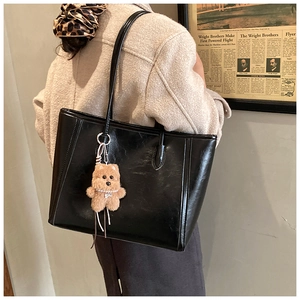 Détail d'un grand sac cabas en cuir noir avec un charmant ours brun porté à l'épaule