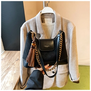Détail du sac en daim noir avec chaîne dorée, pompon marron et logo de marque