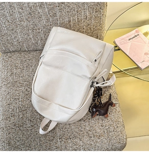 Détail d'un sac à dos en cuir souple beige avec un petit pendentif de chien marron