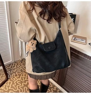 Detail of matte black hobo bag with a cute plush bear charm on a soft interior background