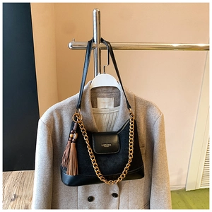 Détail du sac hobo en daim noir avec chaîne dorée et gland sur un manteau de laine grise