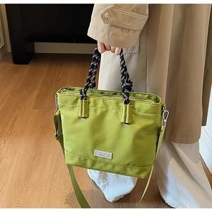 Détail du cabas Oxford vert avec poignée en corde tressée et texture nylon sur manteau beige
