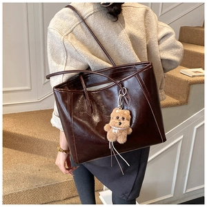 Close-up of a glossy dark brown leather tote bag with a cute plush bear charm detail