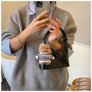 Détail d'un sac demi-lune en cuir verni noir avec un petit ours en peluche marron attaché