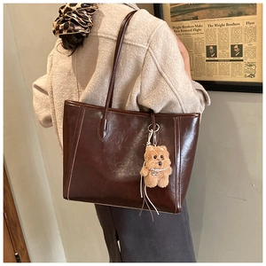 Close-up of a large coffee brown glossy leather tote bag featuring a cute plush dog charm