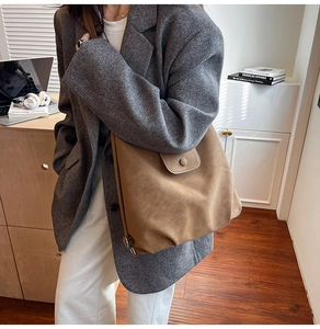 Woman in grey blazer holding a large camel suede tote bag in a modern office setting