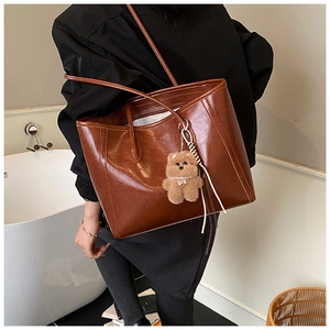 Detail view of a large brown faux leather tote bag with a cute plush bear charm on shoulder