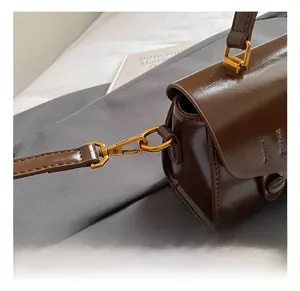 Detail of gold metal hook and stitching on brown glossy leather shoulder bag