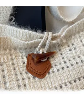 Detail of a beige knitted tote bag featuring a diamond crochet pattern and horn button closure