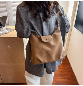 Detail of vintage brown matte leather tote bag with flap and button on a wooden desk