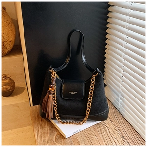 Détail d'un sac en daim noir matelassé avec chaîne dorée et élégant pompon décoratif
