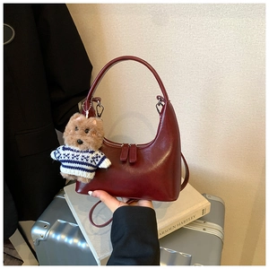 Détail du sac croissant bordeaux avec breloque ours en peluche sur une valise grise