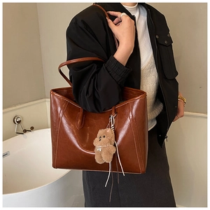 Close-up of vintage brown tote bag with glossy leather texture and plush bear charm
