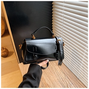 Close-up of black glossy leather handbag featuring wavy flap and gold hardware detail