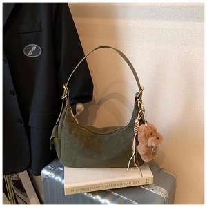 Detail of dark green hobo bag with teddy bear charm and tassel on travel luggage