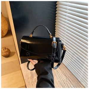 Close-up of black handbag with golden metal buckles and matte leather texture detail