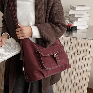Detail view of burgundy leather tote bag with front metal buckle pocket in autumn setting