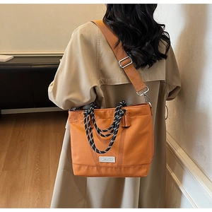 Détail du sac cabas en toile orange-marron avec poignées tressées porté avec un trench beige
