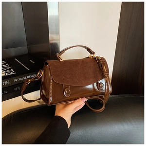 Detail of dark brown leather handbag with contrast textures and round metal buckles
